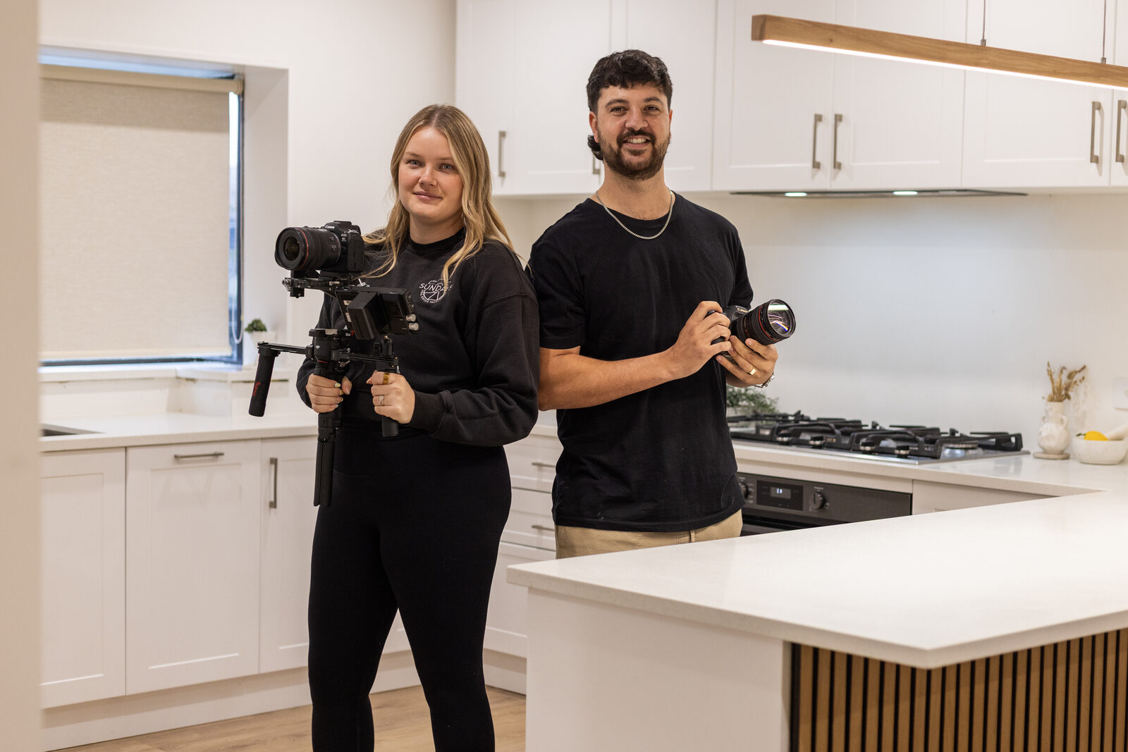 Lisa and Shayn of Sundays Real Estate with their camera and gimbal in a modern kitchen