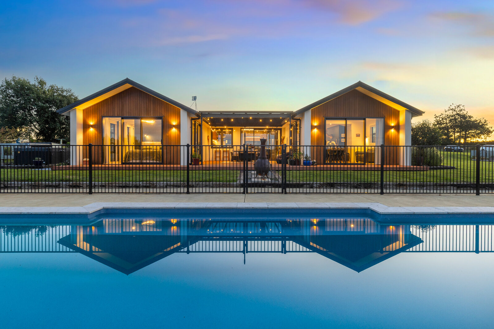 Twilight, single-level home glowing beside a lit pool